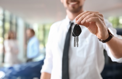 Salesman with car keys in auto dealership, closeup