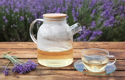 Tasty herbal tea and fresh lavender flowers on wooden table in field