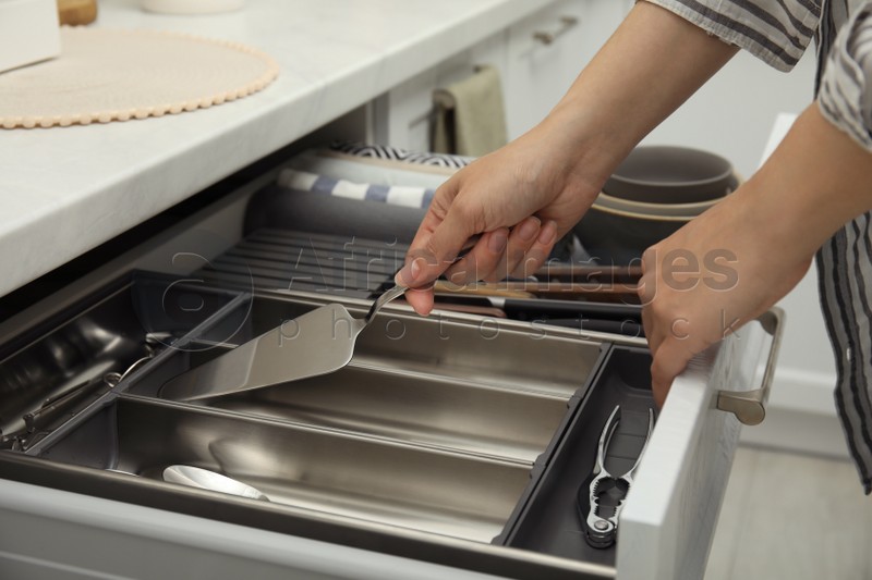 Photo of Woman taking spatula from open drawer of kitchen cabinet, closeup