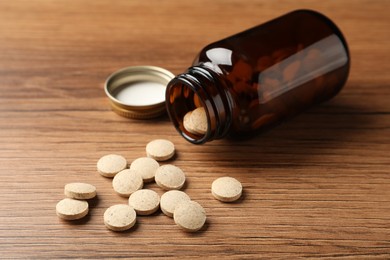 Overturned bottle with dietary supplement pills on wooden table
