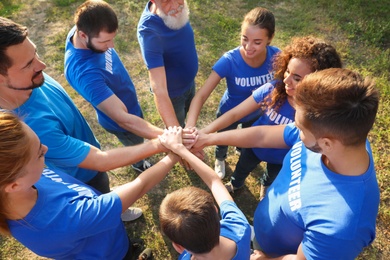 Group of volunteers joining hands together outdoors, above view