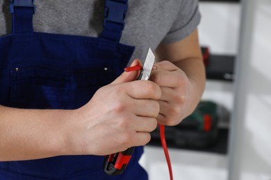 Photo of Professional electrician in uniform stripping wiring indoors, closeup