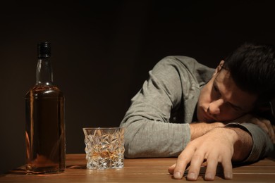 Addicted man and alcoholic drink at wooden table against dark background, focus on glass