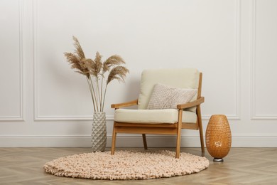 Stylish armchair with cushion, spikes and lamp near white wall indoors. Interior design