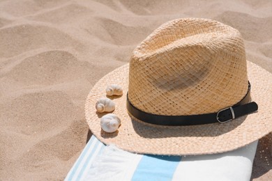 Straw hat with seashells and beach towel on sand, space for text
