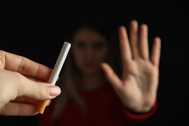 Woman refusing cigarette against black background, focus on hand. Quitting smoking concept