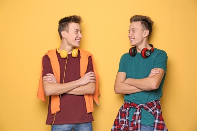Teenage twin brothers with headphones on color background