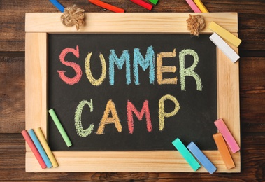 Little blackboard with text SUMMER CAMP chalked in different colors on table, top view