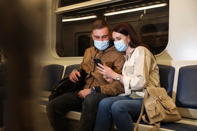 Couple with mobile phone wearing medical masks in subway train. Public transport