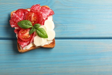 Photo of Tasty toast with butter, salami, tomato, cheese and basil on light blue wooden table, top view. Space for text