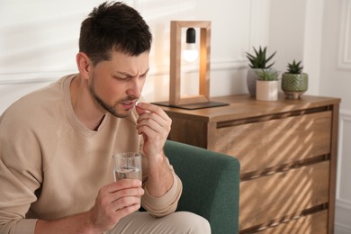 Man with glass of water taking pill at home. Suffering from terrible migraine