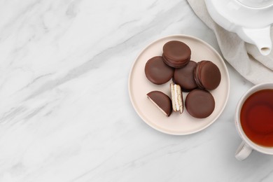 Plate with delicious choco pies and cup of tea on white marble table, flat lay. space for text