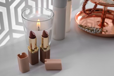 Burning soy candle and lipsticks on white table indoors