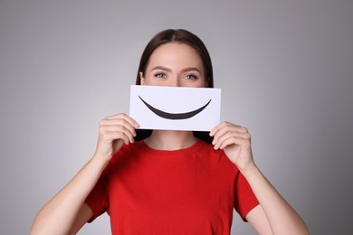 Woman holding sheet of paper with smile on grey background
