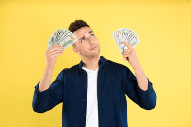 Thoughtful man with cash money on yellow background