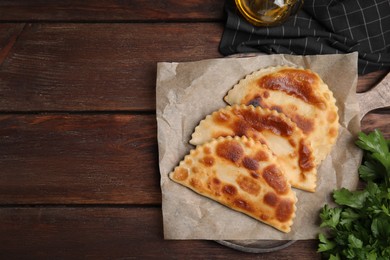 Board with delicious fried chebureki and parsley on wooden table, flat lay. Space for text