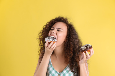 Beautiful African-American woman with donuts on yellow background