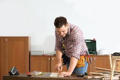 Handsome working man making marks on timber at table indoors. Home repair
