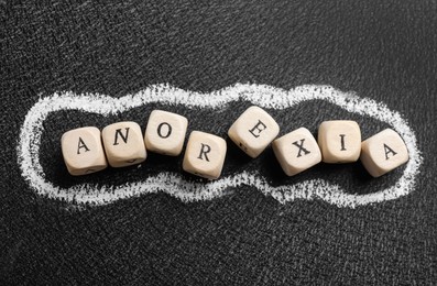 Word Anorexia made of wooden cubes on blackboard, flat lay