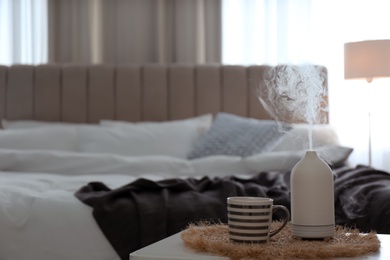 Aroma oil diffuser and cup of tea on table in bedroom. Space for text