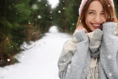 Young woman in snowy conifer forest, space for text. Winter vacation