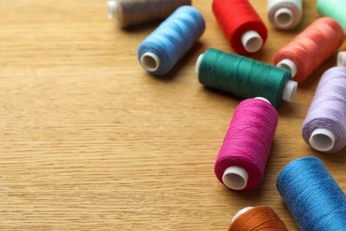 Many colorful sewing threads on wooden table. Space for text