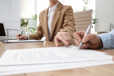 Businesspeople signing contract at table in office, closeup