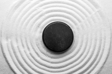 Black stone on sand with pattern, top view. Zen, meditation, harmony