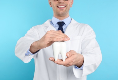 Male dentist holding tooth model on color background, closeup