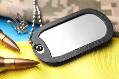 Military ID tag near Ukrainian trident, bullets and camouflage fabric on national flag of Ukraine, closeup