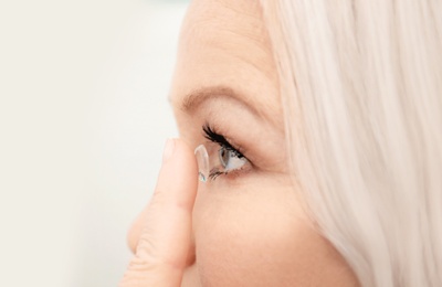 Senior woman putting contact lens in her eye indoors