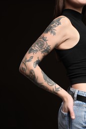 Beautiful woman with tattoos on arm against black background, closeup