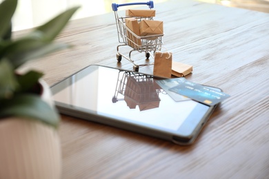 Internet shopping. Small cart with boxes, bags and credit cards near modern tablet on wooden table