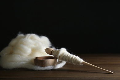 Soft white wool and spindle on wooden table against black background, space for text