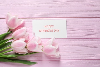 Tulips and greeting card with phrase "Happy Mother's Day" on wooden background
