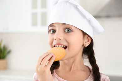 Cute little girl wearing chef hat eating cookies in kitchen