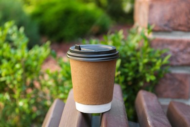 Disposable paper cup with plastic lid on wooden bench outdoors