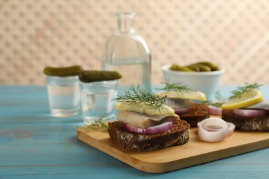 Photo of Delicious sandwiches with salted herring, lemon, onion rings and dill on light blue wooden table. Space for text