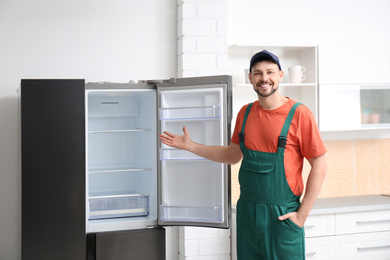 Male technician in uniform near refrigerator indoors
