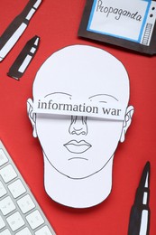 Photo of Information warfare concept. Human blinded with propaganda in media field. Flat lay composition paper cutouts and keyboard on red background