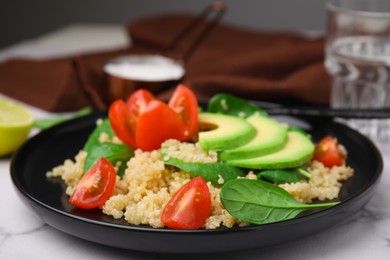 Photo of Delicious quinoa salad with tomatoes, avocado slices and spinach leaves served on white marble table