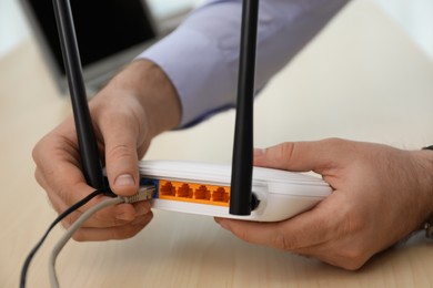 Man connecting cable to router at wooden table, closeup. Wireless internet communication