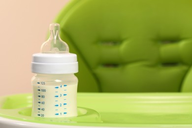 Photo of High chair with feeding bottle of infant formula on light green tray, closeup. Space for text