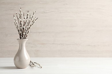 Beautiful pussy willow branches in vase on white wooden table, space for text