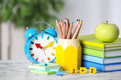 Alarm clock, apple and school stationery on white marble table