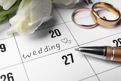 Photo of Calendar with date reminder about Wedding Day, pen and rings, closeup