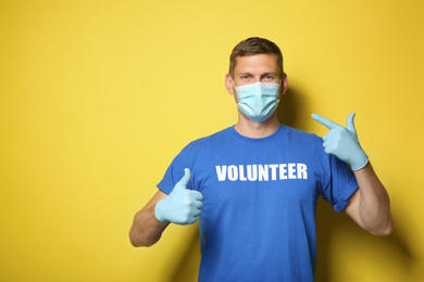 Male volunteer in mask and gloves on yellow background, space for text. Protective measures during coronavirus quarantine