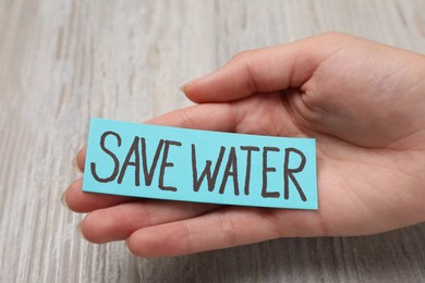 Photo of Woman holding card with words Save Water on wooden background, closeup