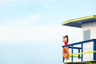 Female lifeguard with binocular on watch tower against blue sky