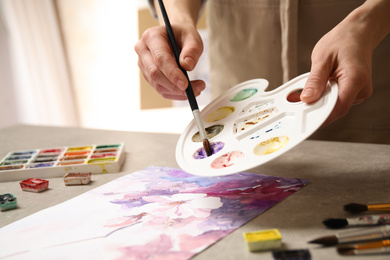 Woman painting flowers with watercolor at grey stone table in workshop, closeup